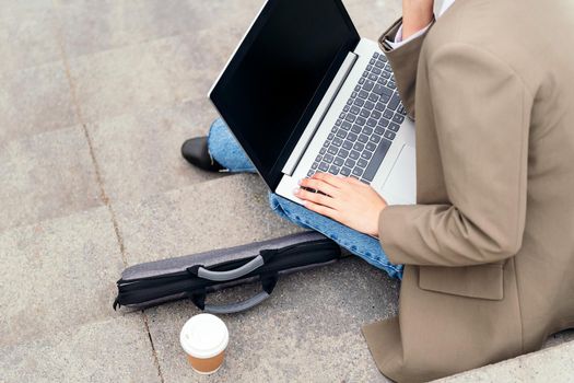 unrecognizable person working with laptop computer sitting on a staircase in the city, concept of business and urban lifestyle, copy space for text