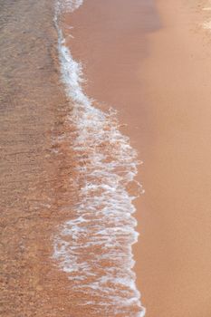 A soft wave runs on a sandy shore on a summer day. Empty space can be used as background for display or montage your top view products.