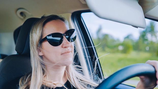 A young woman in a good mood behind the wheel of a car