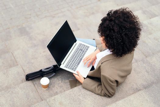 unrecognizable young woman working with laptop computer sitting on a staircase in the city, concept of business and urban lifestyle, copy space for text