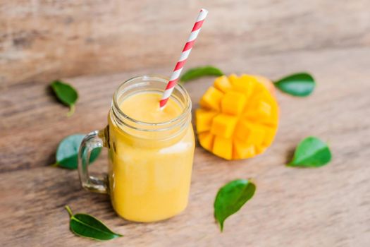 Juicy smoothie from mango in glass mason jar with striped red straw on old wooden background. Healthy life concept, copy space.