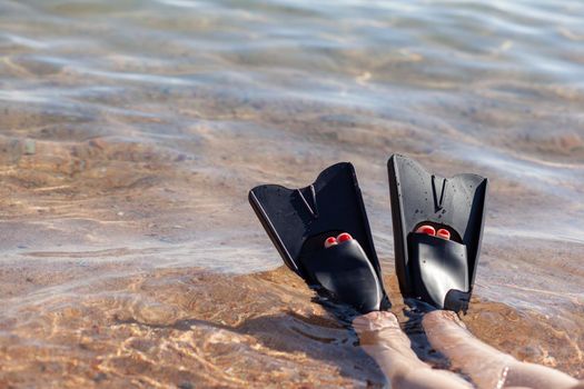 A woman in black flippers splashes near the shore. Fins stick out of the water. Swimming equipment. Summer holidays, fun, exploring the sea world concept. Space for copy.