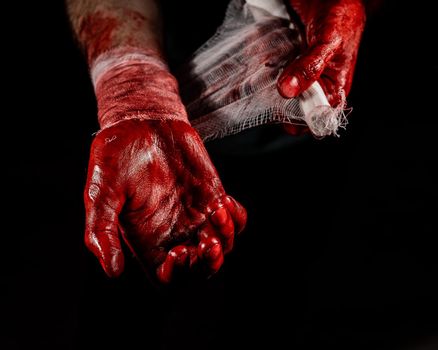 A man covered in blood bandages his hands