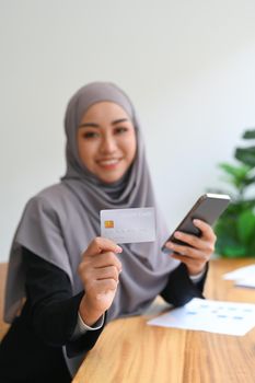 Smiling young Muslim woman holding credit card and mobile phone. Online shopping, internet banking concept.