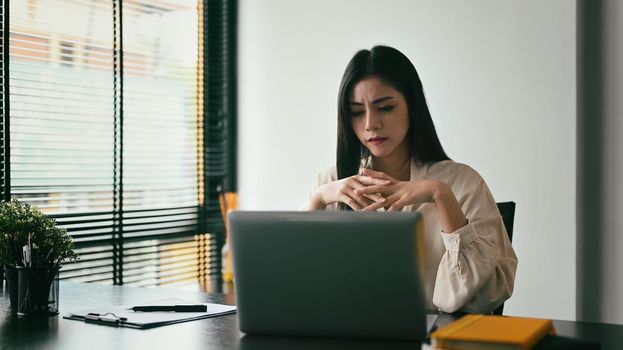 Frustrated female employee looking at laptop, having problem online or email notification.