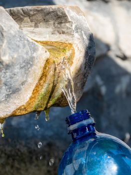 Drink spring water pouring in to bottle over sunlight and natural background in Italy