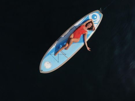 Young attractive brunette woman in red swimsuit, swimming on kayak around volcanic rocks, like in Iceland. Back view. Christmas holiday vacation and travel concept.