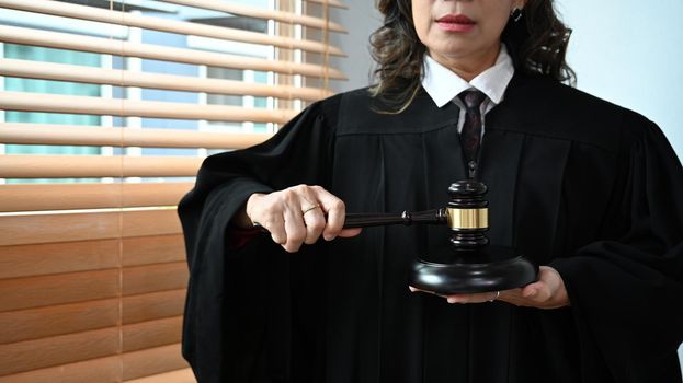 Confident senior judge in robe gown uniform holding a gavel in hands. Lawyer, justice and law and attorney concept.