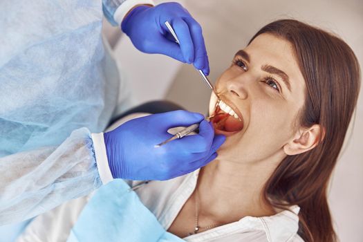 Professional doctor is doing tooth surgery to happy caucasian woman in modern dental cabinet