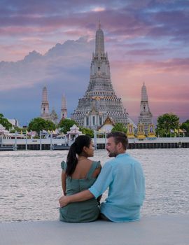 Out of focus blur couple of Asian women and European men watching the sunset at Wat Arun temple in Bangkok Thailand, Temple of Dawn, Buddhist temple alongside the Chao Phraya River.