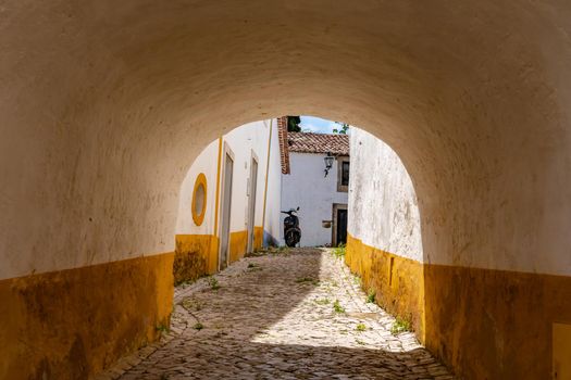 View of a cobbled backyard with access through the thick ramparts of the fortress in Obidos, Portugal