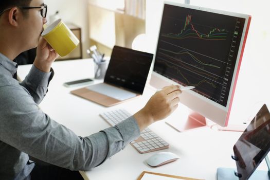 Investment professionals point their pen at their computer monitor to analyze the stock market for profit