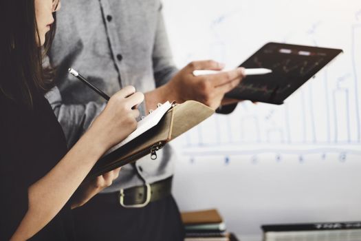 Woman using pen for note with An investment expert points a pen at a tablet monitor to analyze the stock market to teach you how to make a profit