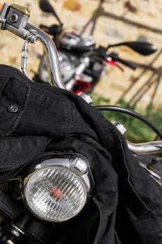 Black denim jacket thrown on the handlebars of a motorcycle close up