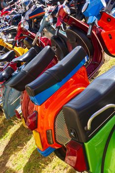 Row of brightly colored mopeds parked on the grass on a sunny day