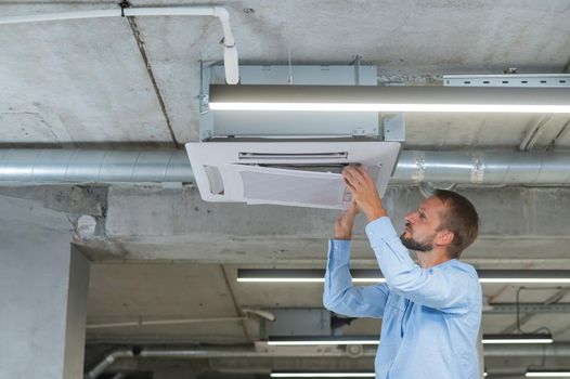 Caucasian bearded man repairing the air conditioner in the office