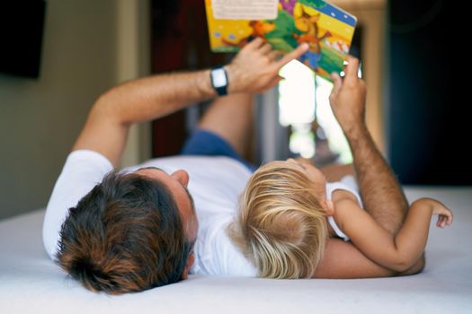 Dad shows his daughter a book with pictures lying on the bed. High quality photo