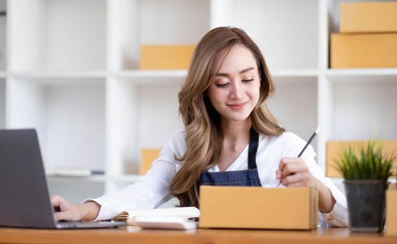 Portrait of Asian young woman SME working with a box at home the workplace.start-up small business owner, small business entrepreneur SME or freelance business online and delivery concept..