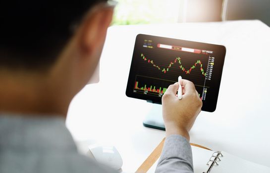 Investment professionals point their pen at their computer monitor to analyze the stock market for profit