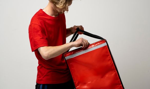 Delivery guy employee man in red uniform work as dealer courier hold red thermal food bag backpack. Food delivery service