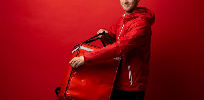 Young courier with thermo bag on red background, space for text. Food delivery service