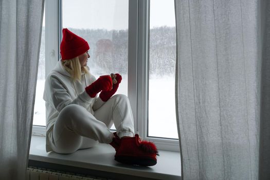 A woman in a white suit sits on the windowsill and looks out the winter window. High quality photo