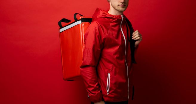 Delivery employee man in red uniform and thermal food bag backpack work courier service on red background studio