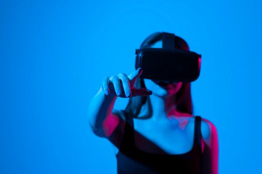 Excited young woman in VR headset exploring artificial computer world or playing video game at home and touching something in virtual reality