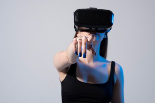 Young attractive woman wearing black top and vr helmet is standing and touching air. Concept of modern technology and virtual reality
