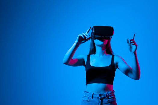 Young brunette woman wearing virtual reality device, vr glasses and playing a game with a friends online in neon light