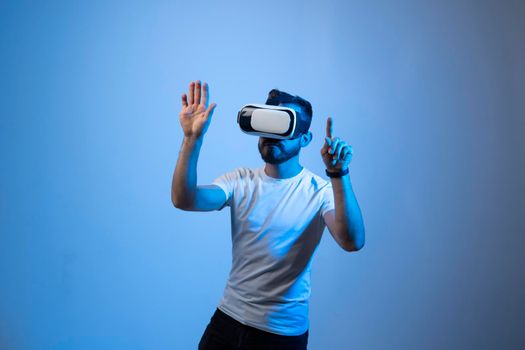 Serious millennial male student in white t-shirt and vr glasses moves his hands manipulating gestures in virtual reality world. 3d technology, virtual reality and entertainment concept