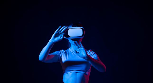 Young woman wearing vr headset and watching 360 videos in neon light. Girl toching virtual objects in vr glasses