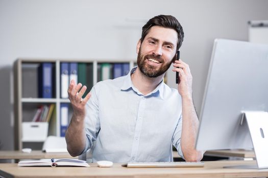 Successful male programmer working in the office at the computer talking to colleagues on the phone smiling.