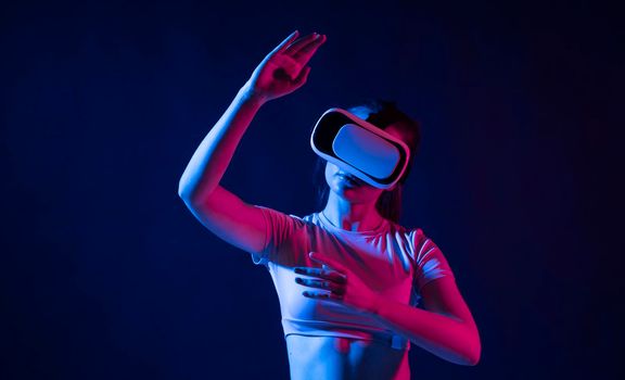 Woman with VR virtual reality goggles trying to touch something with a finger in a metaverse. Futuristic lifestyle. Metaverse technology concept.