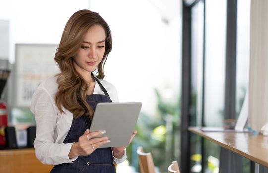 Startup successful small business owner sme beauty girl stand with tablet smartphone in coffee shop restaurant. Portrait of asian tan woman barista cafe owner. SME entrepreneur seller business concept.