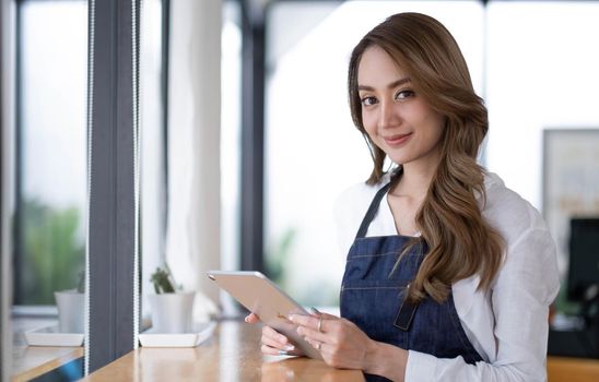 Startup successful small business owner sme beauty girl stand with tablet smartphone in coffee shop restaurant. Portrait of asian tan woman barista cafe owner. SME entrepreneur seller business concept.