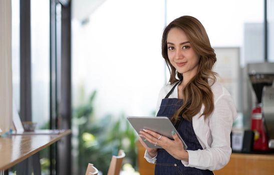 Startup successful small business owner sme beauty girl stand with tablet smartphone in coffee shop restaurant. Portrait of asian tan woman barista cafe owner. SME entrepreneur seller business concept.