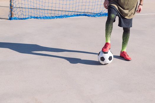 detail of the legs of an unrecognizable football player foot on the ball in a concrete soccer field, concept of healthy lifestyle and urban sport in the city, copy space for text