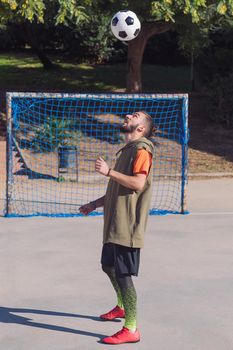 vertical photo of a soccer player playing giving head hits to the the ball in a concrete soccer field, concept of healthy lifestyle and urban sport in the city, copy space for text