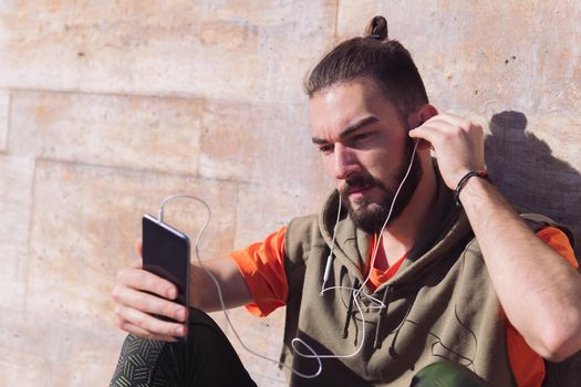 handsome sportsman putting on earphones to listen to music from his smart phone, concept of technology and urban sport lifestyle in the city, copy space for text