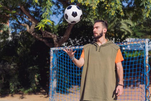 handsome hipster football player in front of the goal of an urban court throwing the ball with the hand, concept of healthy lifestyle and urban sport in the city, copy space for text