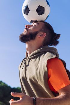 vertical portrait of a football player playing balancing the ball on his head with a clear blue sky in the background, concept of healthy lifestyle and urban sport in the city