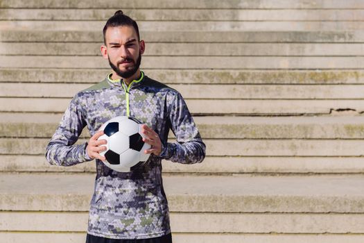 portrait of a handsome sportsman in a concrete soccer court with the football ball in his hands, concept of healthy lifestyle and urban sport in the city, copy space for text