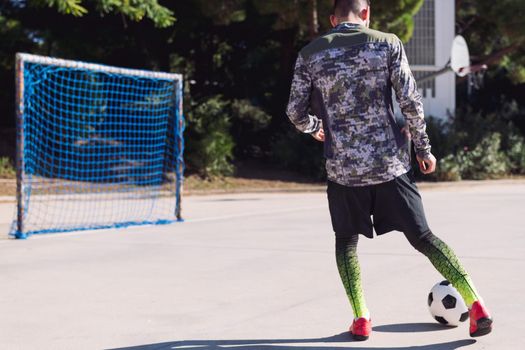 rear view of an unrecognizable football player kicking the soccer ball into an empty goal in a concrete football court, concept of healthy lifestyle and urban sport in the city, copy space for text