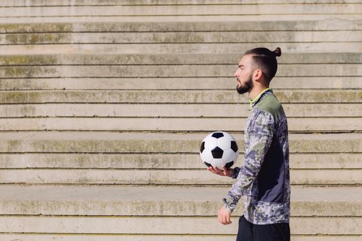 portrait of a sportsman with hair in a bun walking with the ball in his hand on a concrete soccer court, concept of healthy lifestyle and urban sport in the city, copy space for text