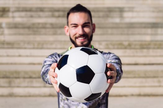 football ball in the hands of a smiling sportsman in a concrete soccer court, selective focus on the ball, concept of healthy lifestyle and urban sport in the city, copy space for text