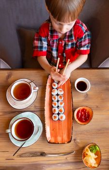 Little cute little boy eating sushi in a cafe, concept of eating. the boy in the restaurant eats sushi, dumbly holding chopsticks. View from aboveHigh quality photo