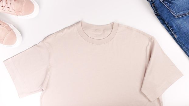 Beige unisex t shirt mock up flat lay on white background. Top front view t-shirt, snikers, jeans and copy space. Mockup t-shirt and summertime. Template blank shirt