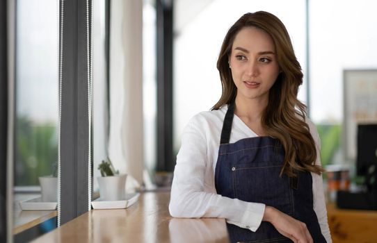 Opening a small business, AHappy Asian woman in an apron standing near a bar counter coffee shop, Small business owner, restaurant, barista, cafe, Online, SME, entrepreneur, and seller concept.