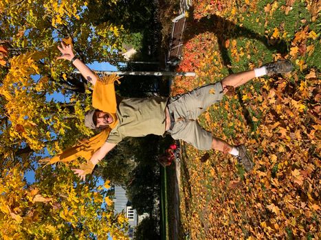 Mature man in yellow scarf jumping in autumn park with yellow leaves